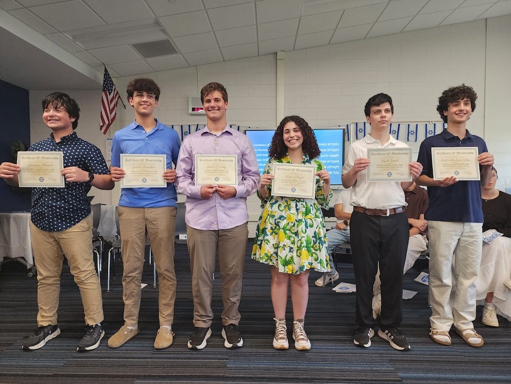 Group of students in a room holding certificates, standing together. An American flag is visible on the wall.