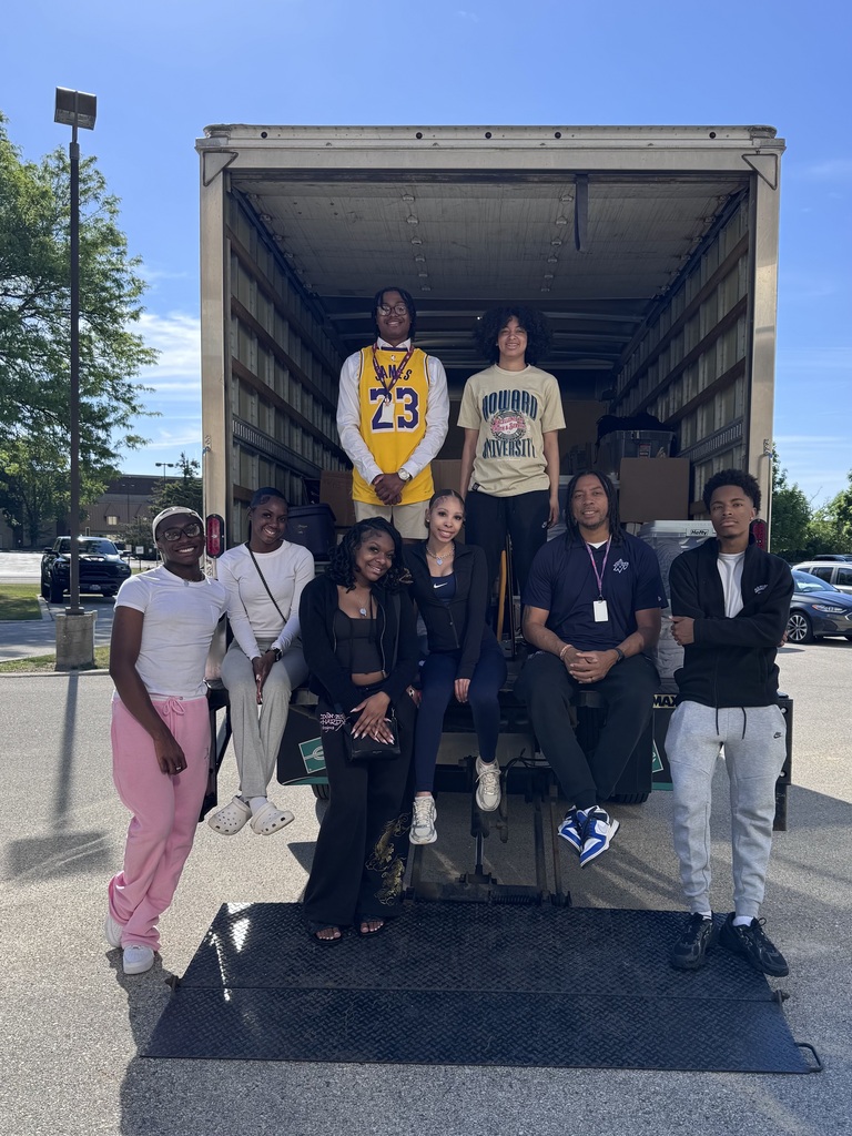 A group of people stands next to a moving truck with a ramp down, some wearing sneakers.