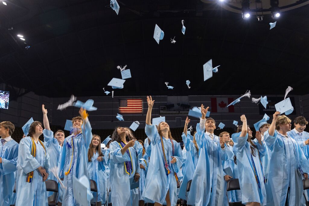 Graduates in blue robes and caps, tossing their caps into the air at a graduation ceremony.