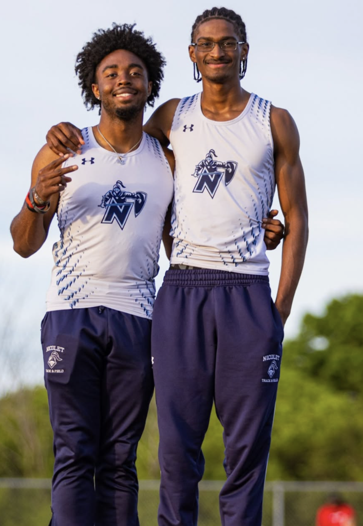 Four young men in matching white shirts and shorts pose on a track, holding a baton.