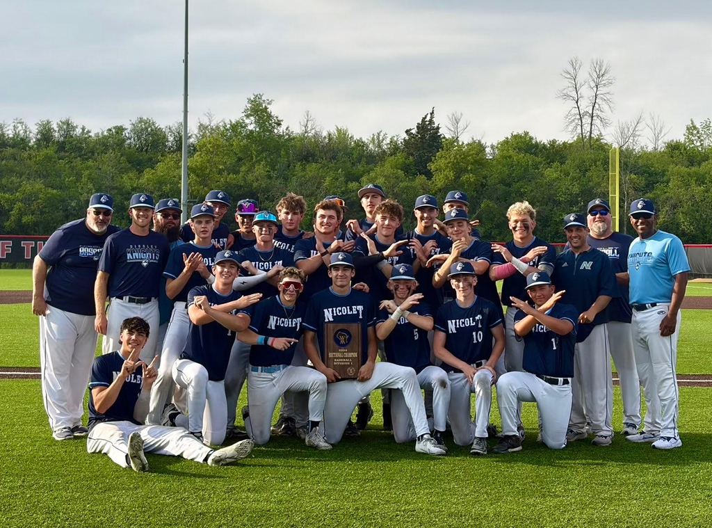 Team in blue jerseys, hats, and sneakers posing for a photo on a field with a trophy.