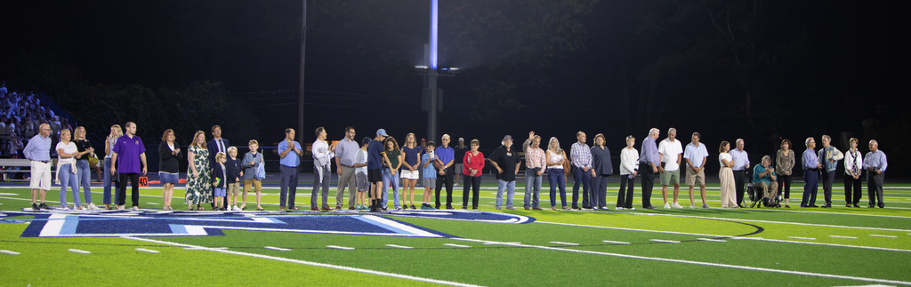 A group of people, dressed in various colors, standing on a football field at night.