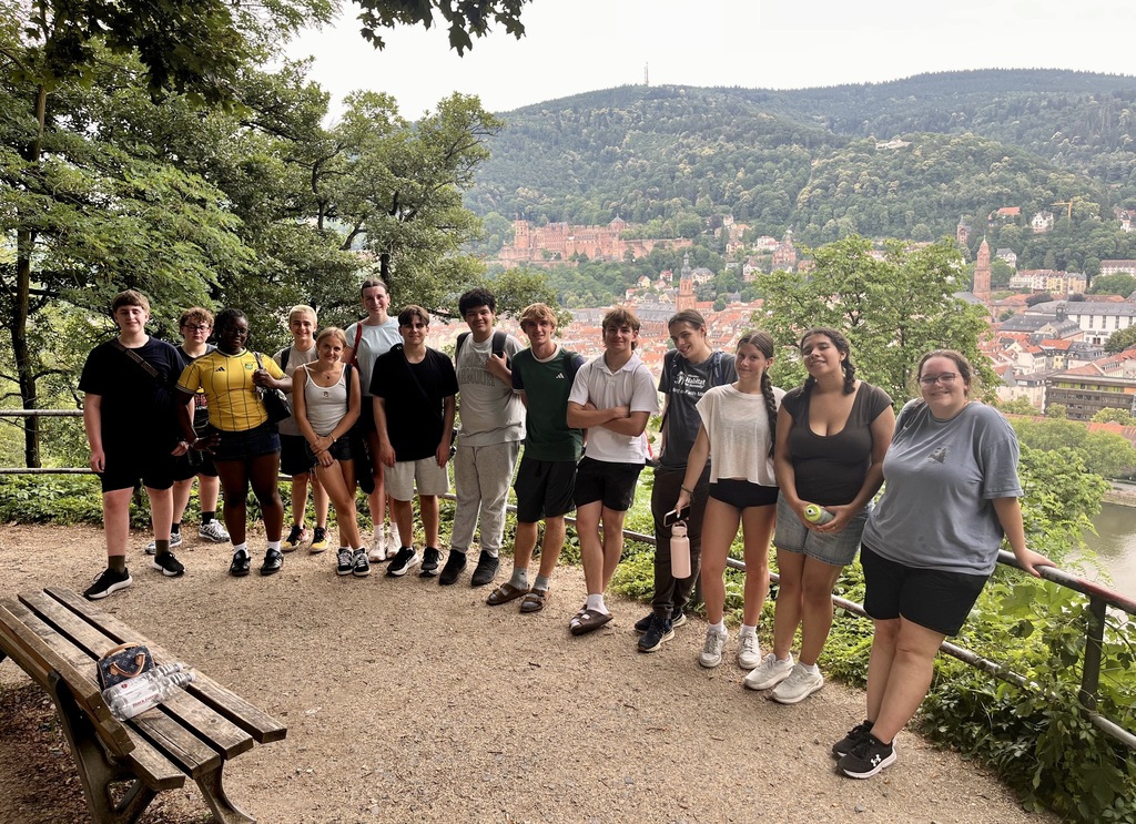 Group of young people in casual clothing stands on a hill, posing for a photo.