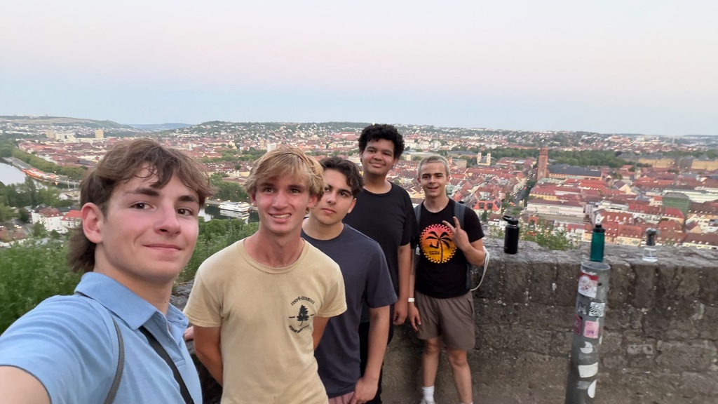 A group of people smiling, standing in front of a city view on a concrete wall.