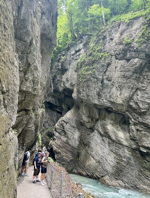A group of people stands near a narrow water channel, with rocky cliffs on either side.