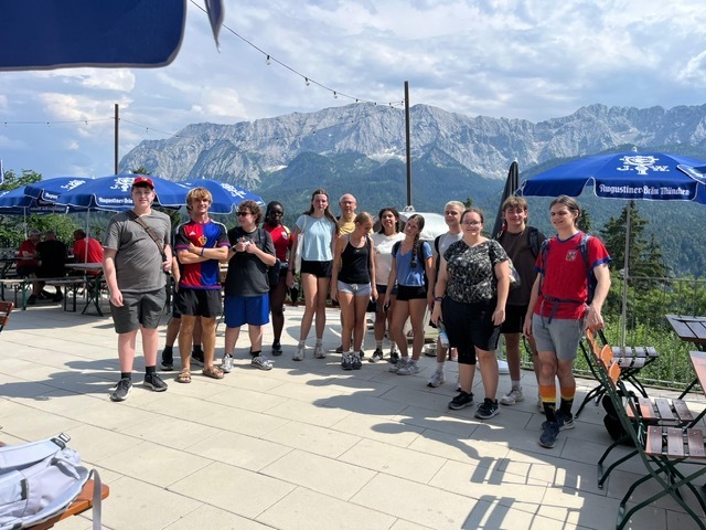 Group of people on a terrace with mountains in the background, some wearing hats and sneakers.