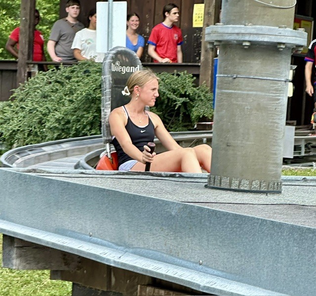 Woman seated on a ride with her feet hanging over the edge, other people standing in the background.