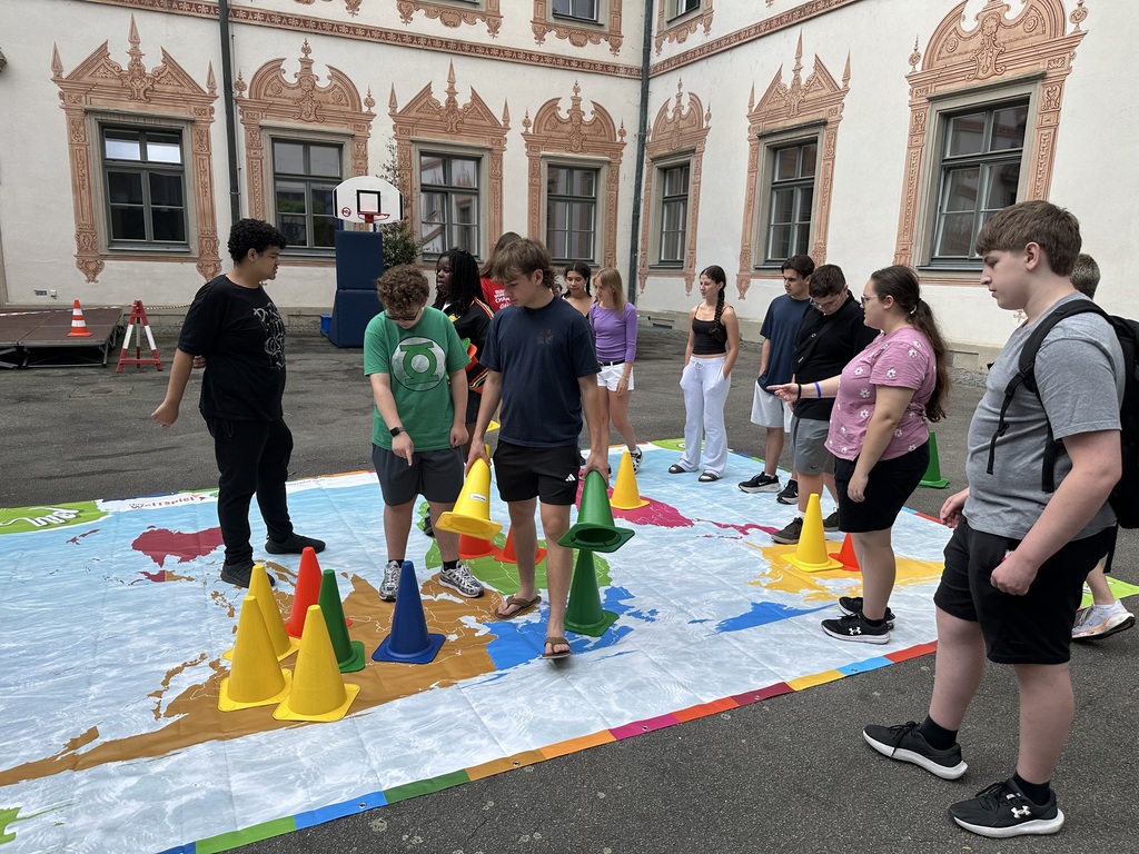 A group of people stand on a colorful map with various-colored cones, wearing sneakers and backpacks.