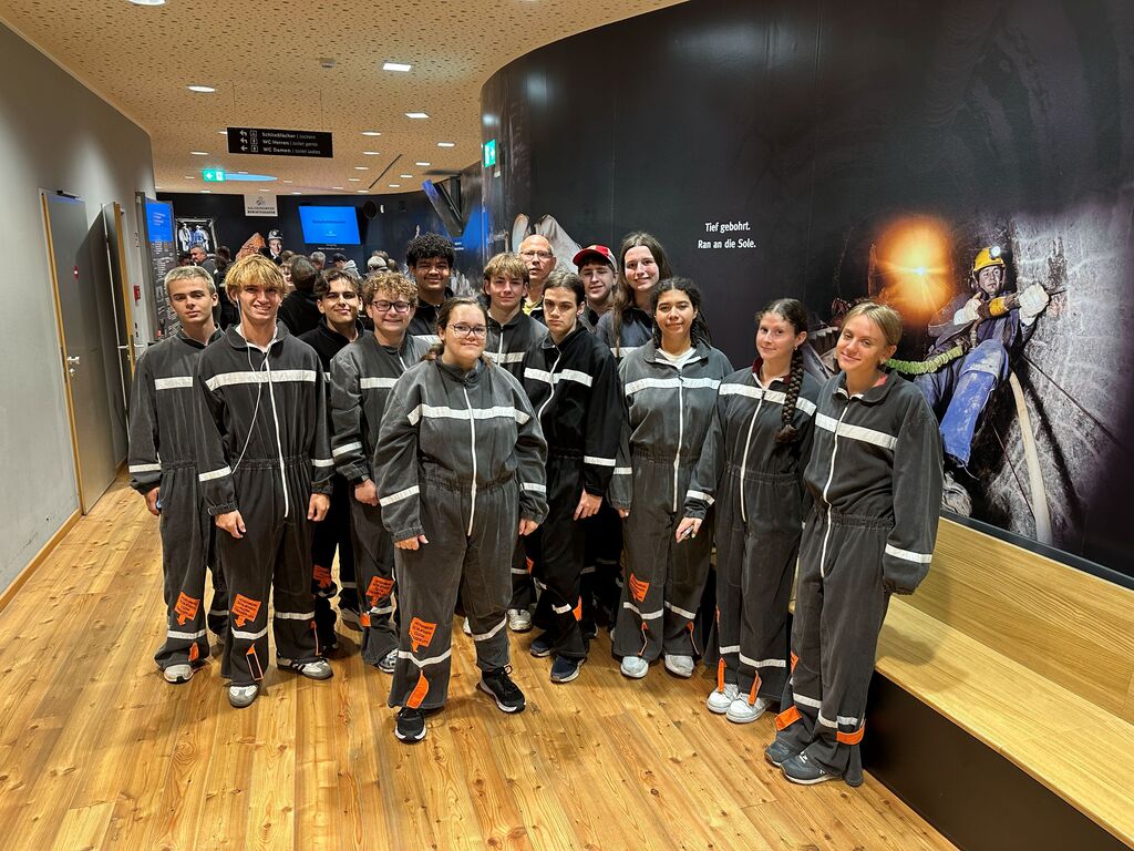 A group of individuals in grey jumpsuits pose in a hallway with a wall mural.