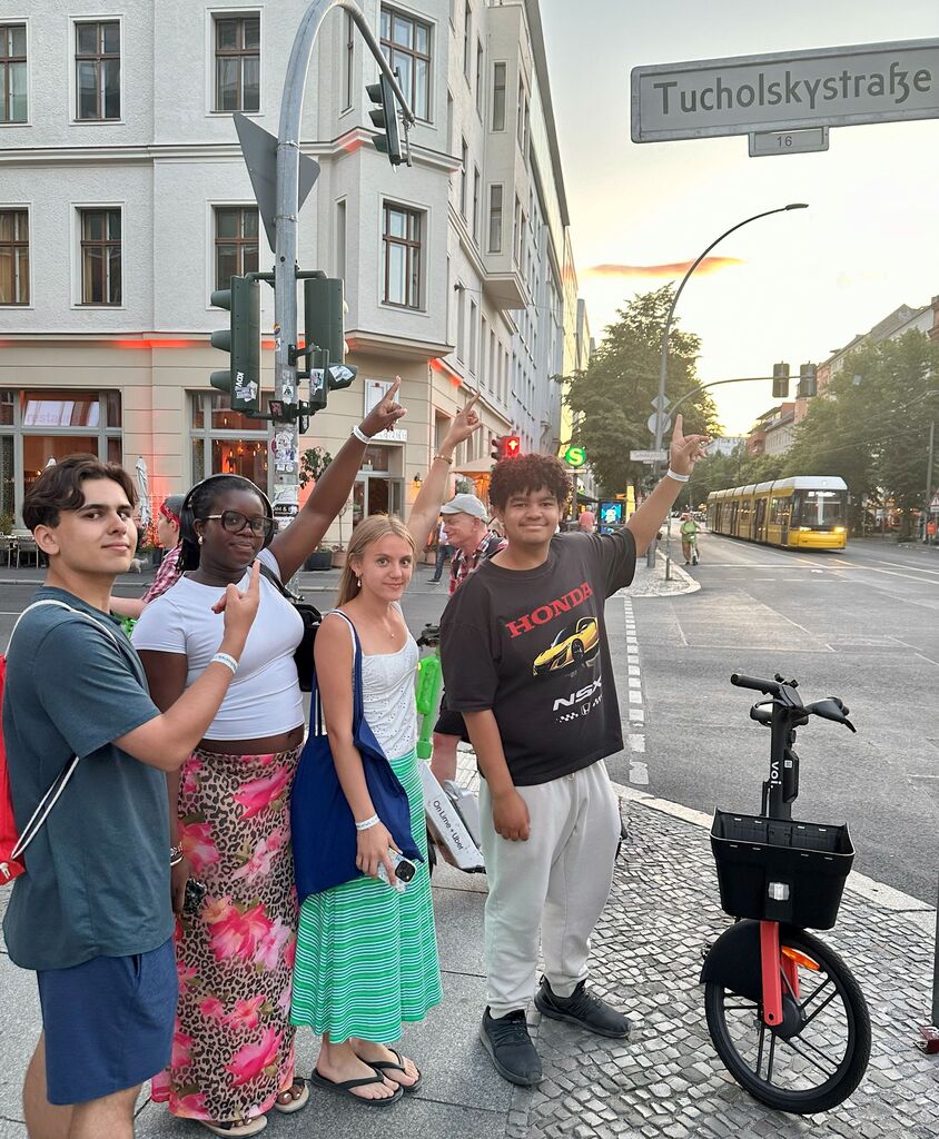 A group of people, some raising their hands, stand in a city, near a bicycle and traffic signs.