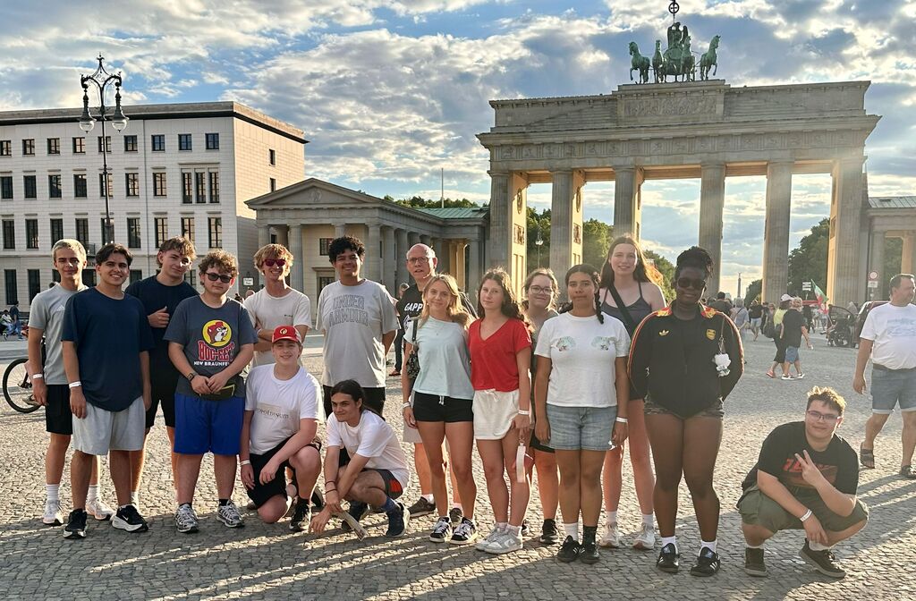 A group of people pose for a photo in front of the Brandenburg Gate with a cloudy sky.