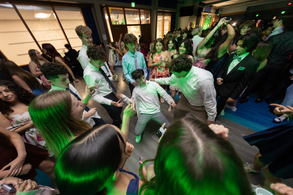 People dance on a dance floor with green lighting. Some wear formal attire.
