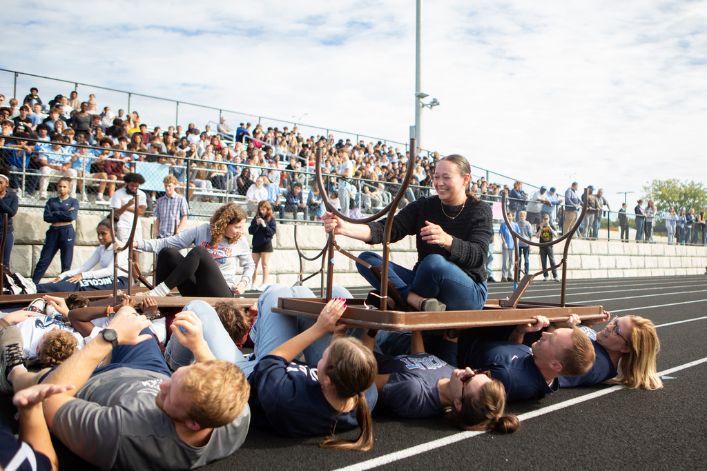 People hold a table over a group of individuals lying on a track while an audience watches.