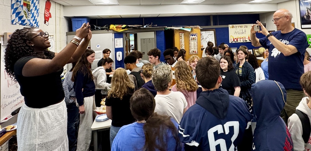 A group of people in a room. Some are standing, some are sitting, and others are raising their hands.