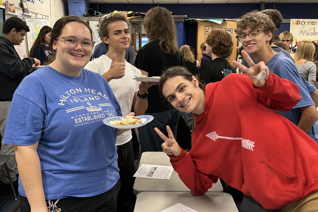 Four teens posing at a school event, one holding a plate of food and another making a peace sign.