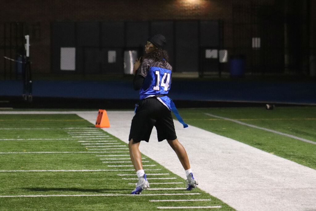 An athlete with number 14 on the jersey throws a ball in an outdoor football field at night.