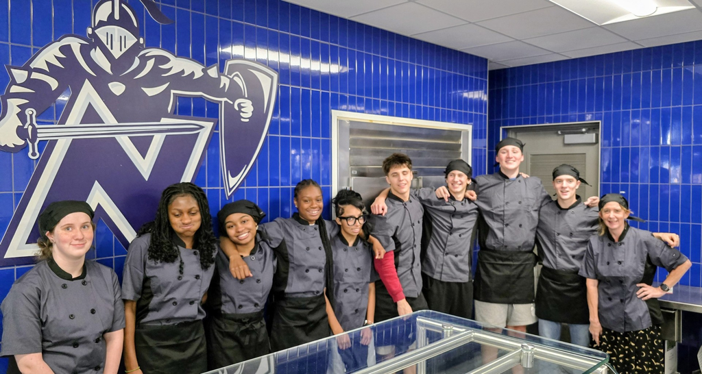 A group of people wearing aprons stands in front of blue tiles with a large 'N' logo.