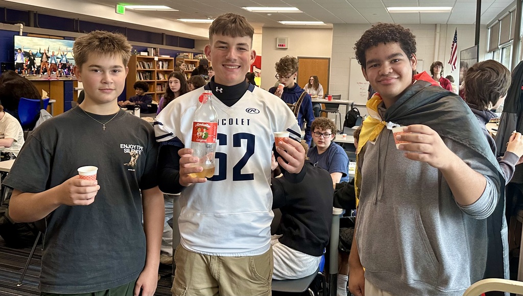 Three boys stand together holding cups. One wears a football jersey with the number 32, another a gray hoodie, and the third a gray t-shirt.