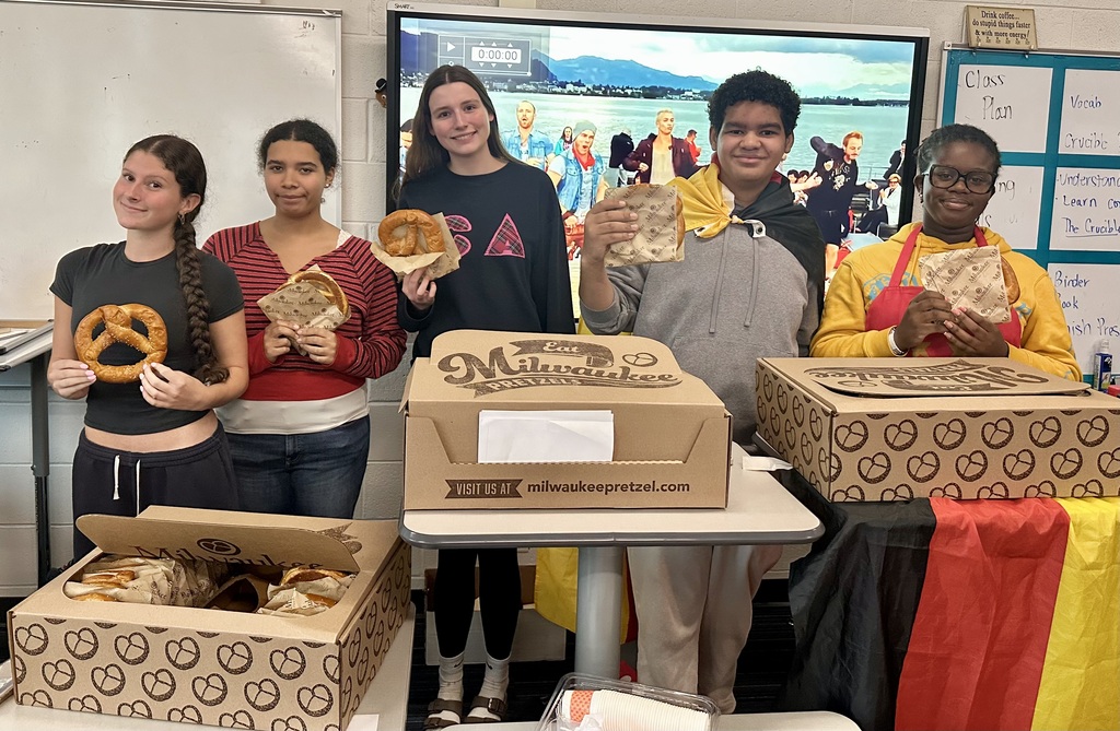 Group of students holding pretzels in front of boxes with one wearing a yellow apron.