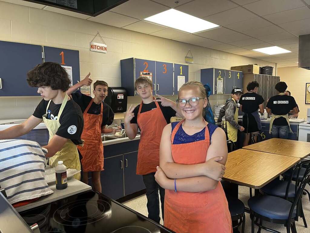 Students in school kitchen cooking and smiling at camera
