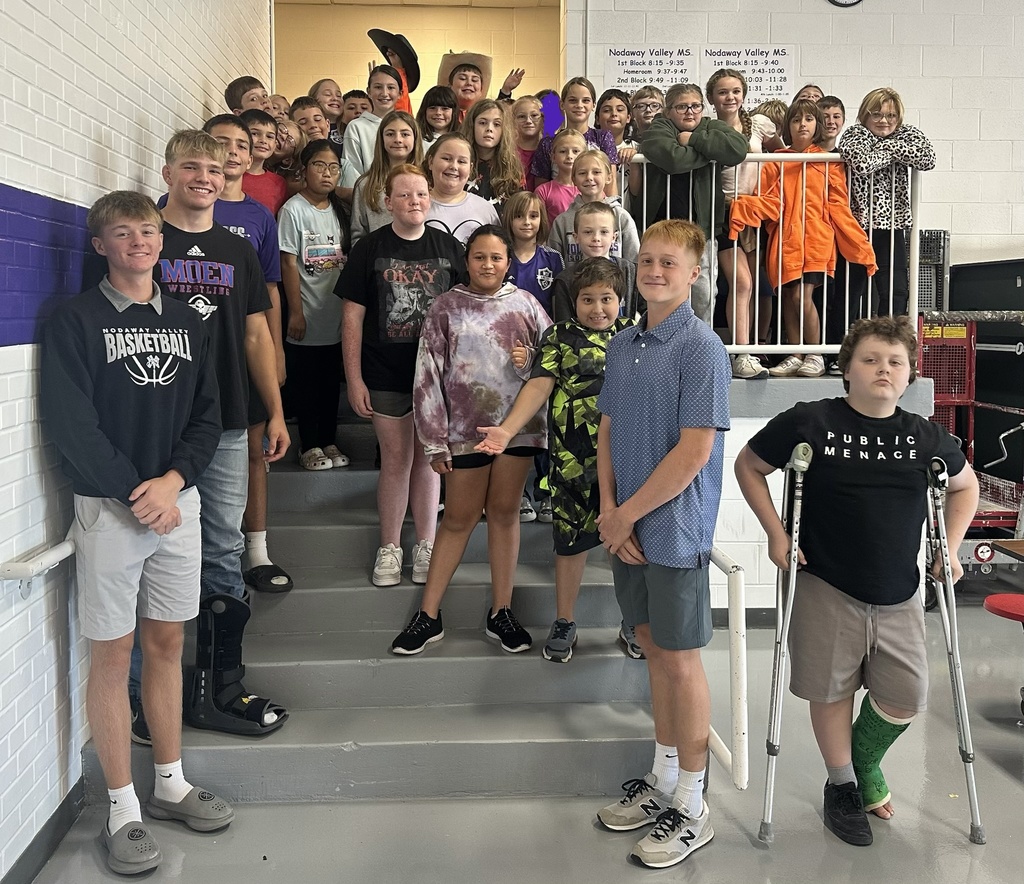 Two high school students pose in front of a group of middle school students on the cafeteria steps.