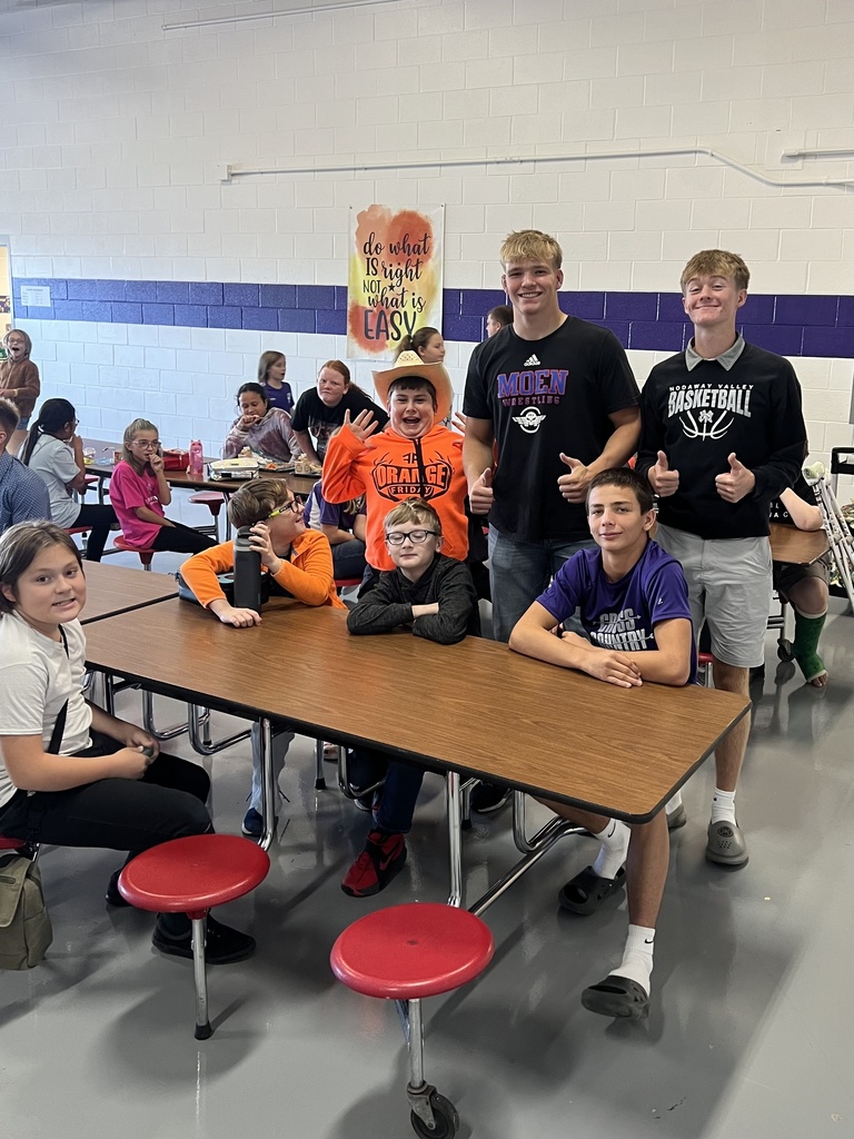 Two high school students pose with middle school students around a cafeteria table during the Homecoming Court’s lunch visit.