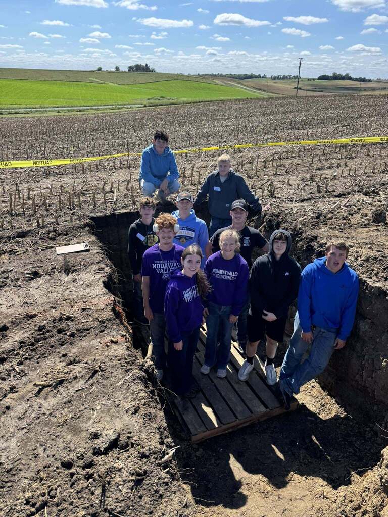 Nine Nodaway Valley students pose together in a soil pit in a harvested field.