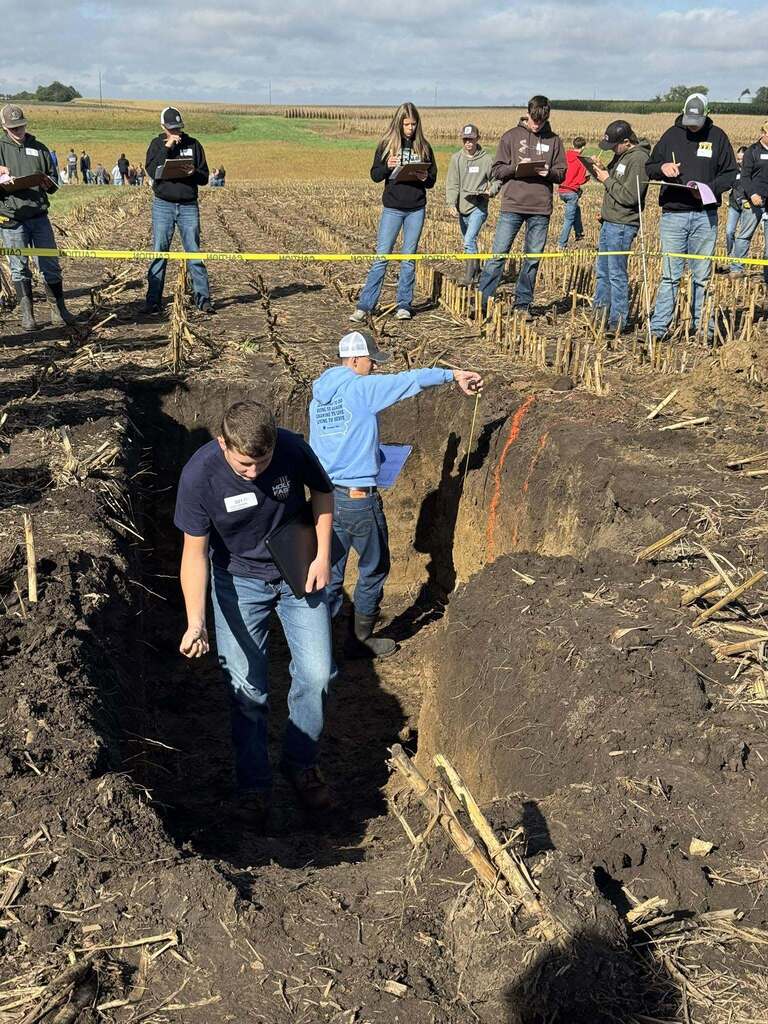 Students stand in a soil pit and examine its layers while others take notes from the edge of the pit.