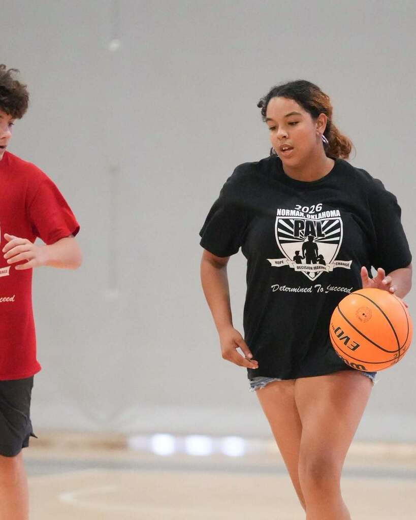 Two people on a basketball court. A person in a red shirt and black shorts. A person in a black shirt and shorts.