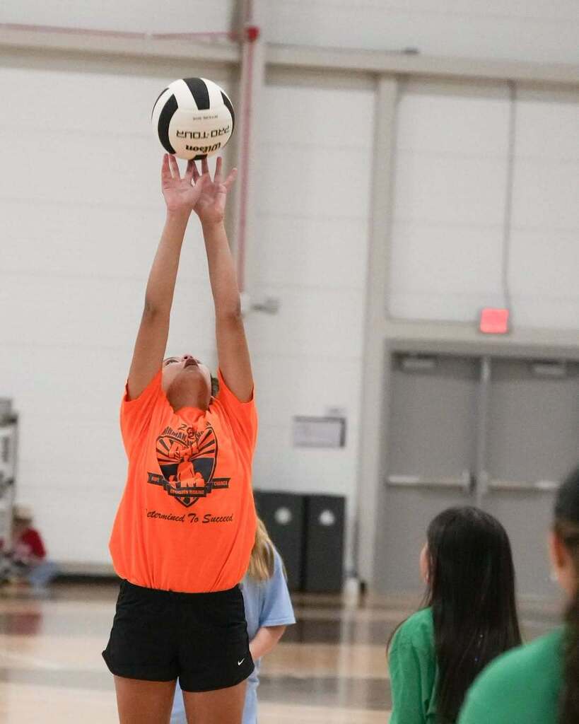 An indoor volleyball player in an orange shirt jumps and prepares to hit a volleyball.