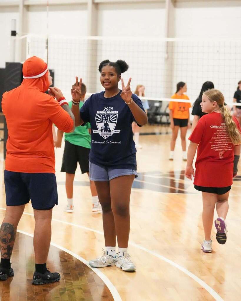 An adult and a girl make peace signs on a basketball court. Others are in the background.