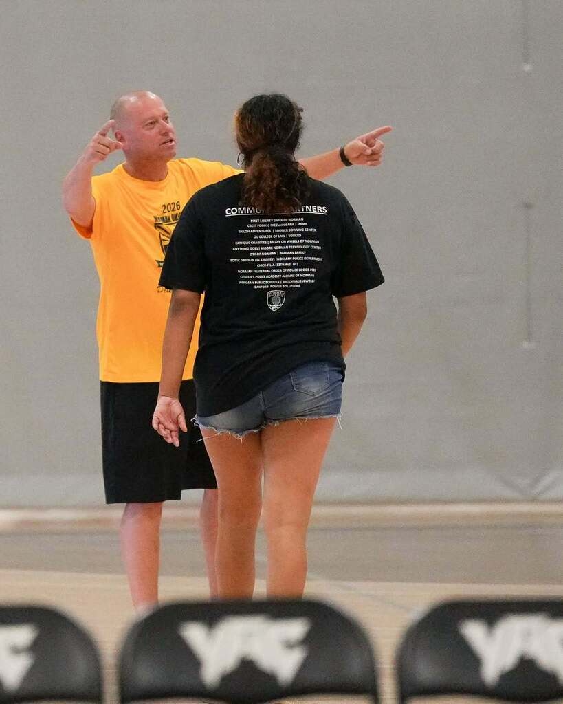 Man in yellow shirt giving instructions to a woman in black shirt and shorts.