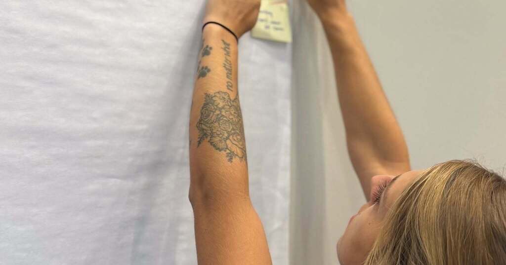 A woman with a tattoo on her left arm stands and stretches her right arm to reach a whiteboard.