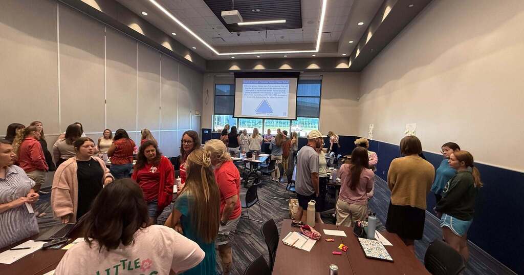 A conference room with many people standing around tables, one with a projector screen.