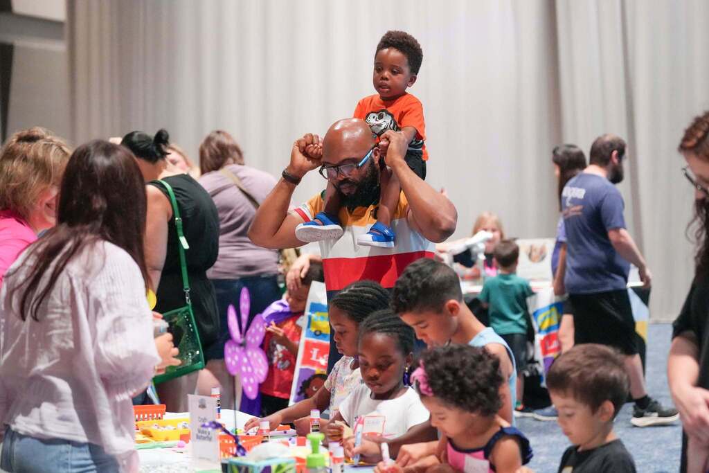 A group of people in a room with tables, where adults interact with children, some standing and others seated.