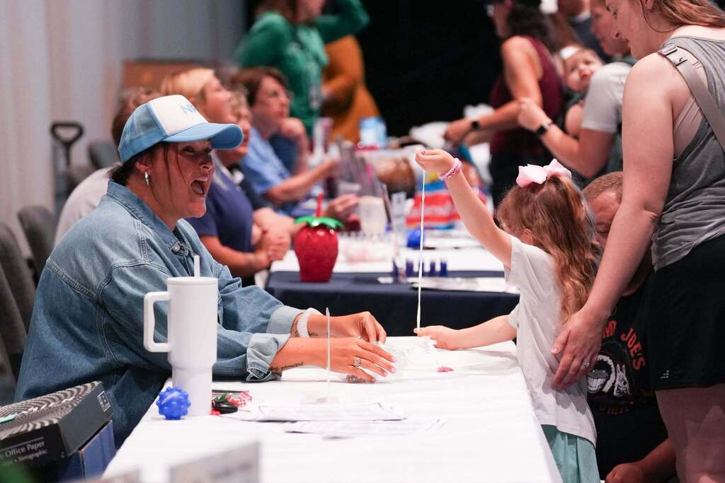 People seated at a table, one woman laughing, another woman with a young girl, red cup on table.