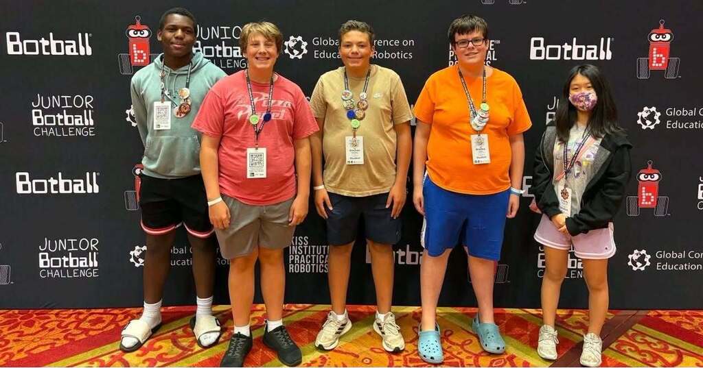 Five individuals wearing t-shirts and sneakers pose for a photo in front of a black backdrop with a red and white logo.