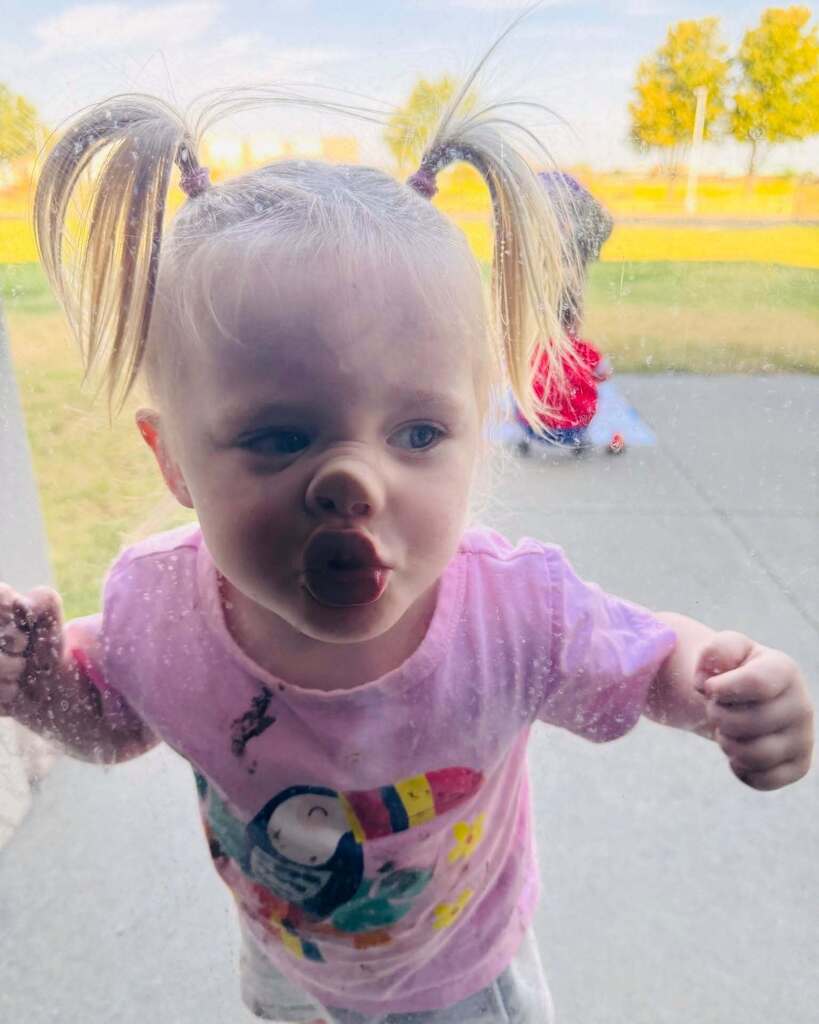 A young girl with pigtails sticks puts her face on the glass.