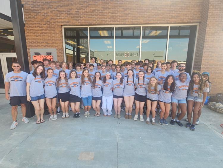 A group of people wearing matching gray T-shirts and shorts stands in front of a brick building.