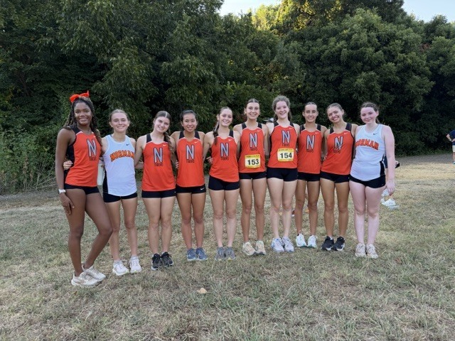 A group of women in orange and white athletic wear pose for a photo on a field.