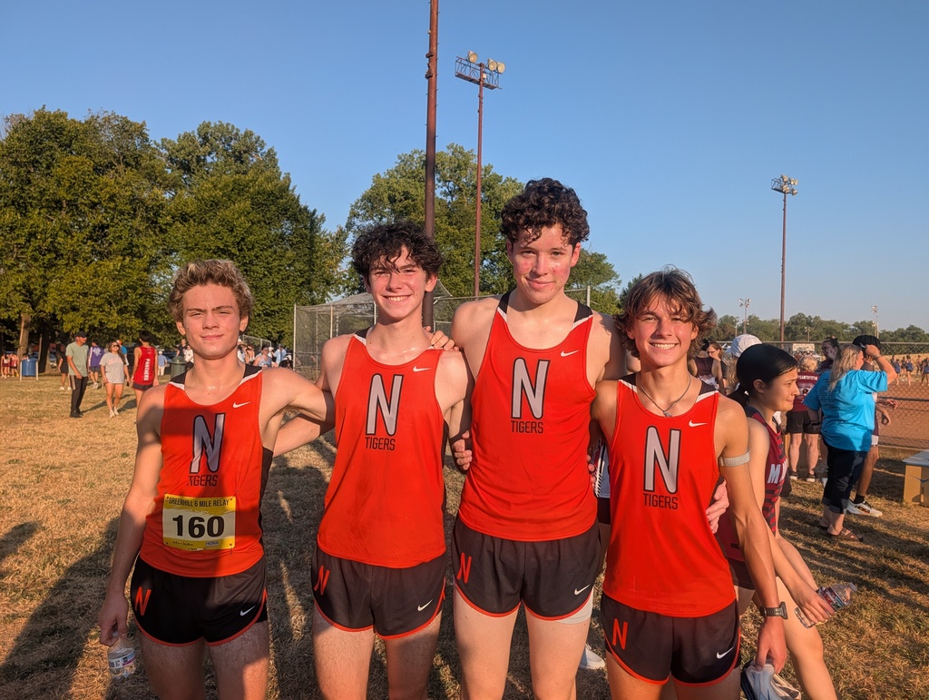 Four young men in matching orange shirts with the letter N and black shorts pose for a photo.