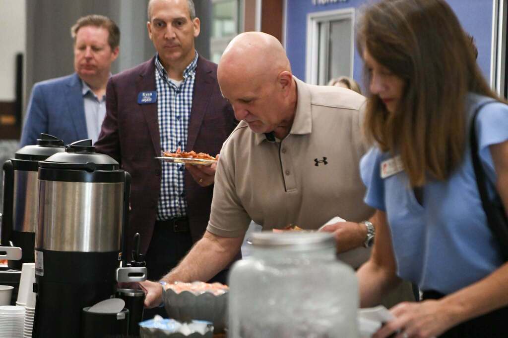 Four adults are standing near a food table. One adult holds a plate of food.