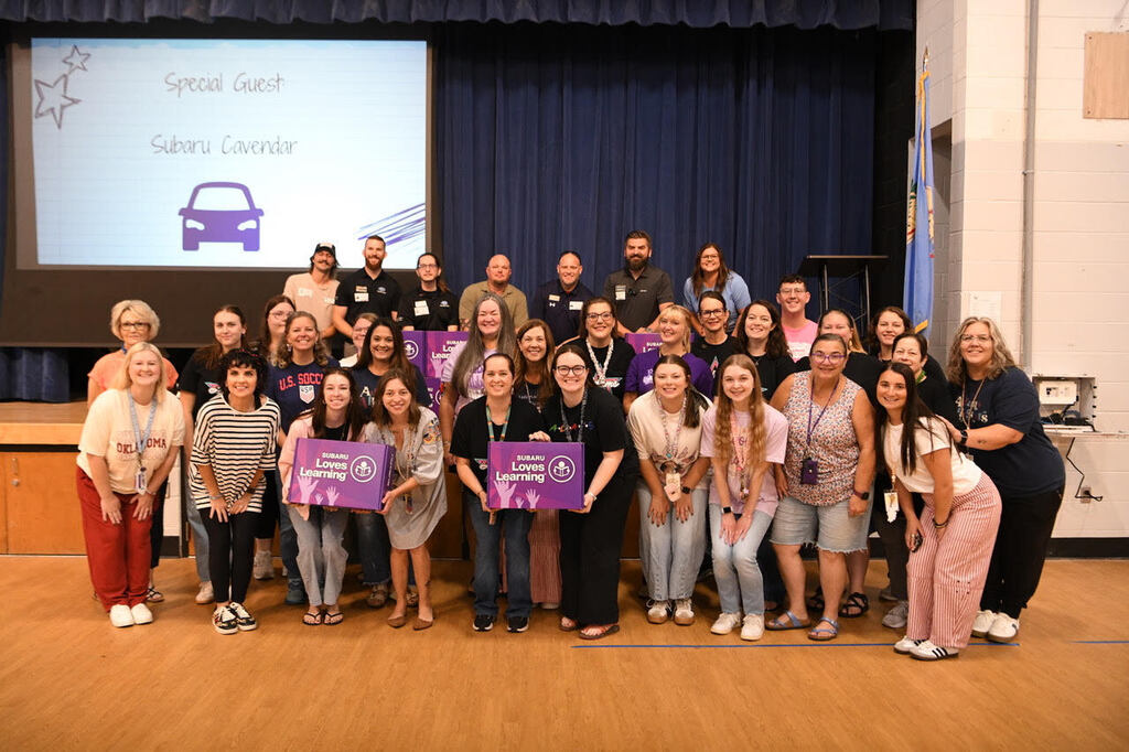 A group of adults and teens poses in front of a projector screen with purple signs.
