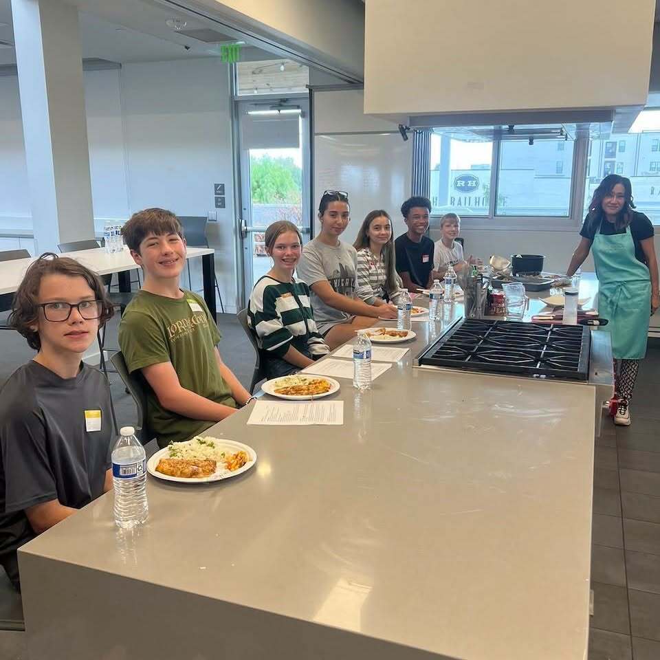 Group of students seated at a kitchen counter, some wearing glasses, with food on plates.
