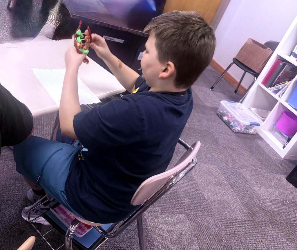 A boy in a dark blue shirt and blue pants sits in a chair holding a small object.