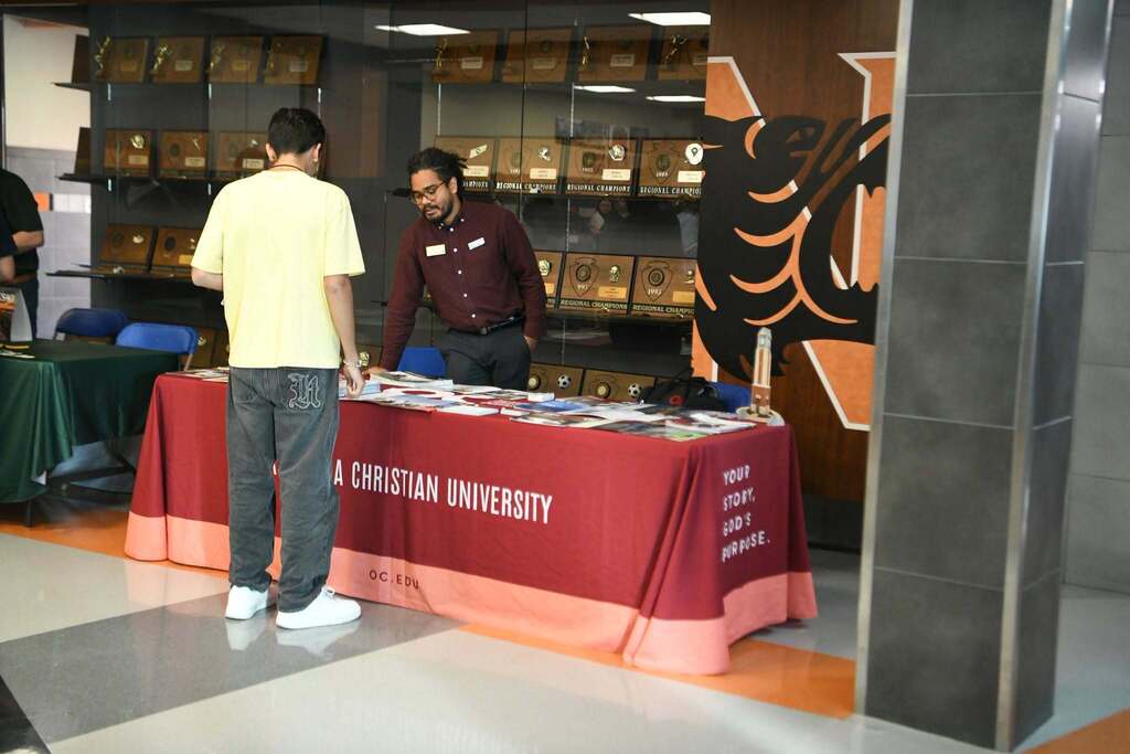 Two people standing by a table with a red tablecloth. A university logo is printed on it.