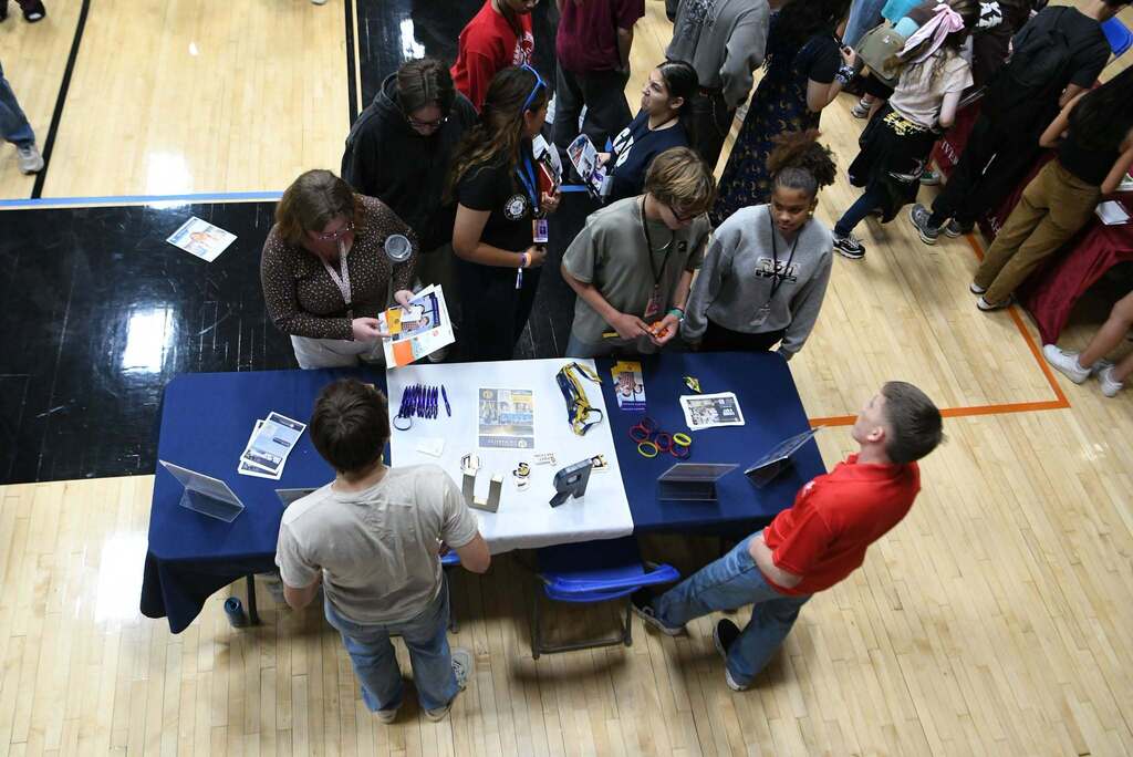 An overhead view of people in a gym. Some are standing, some sitting, and they are all gathered around a table.