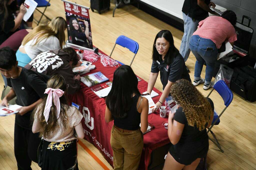 Several individuals gathered around a table with a red cloth, papers, and a woman standing.