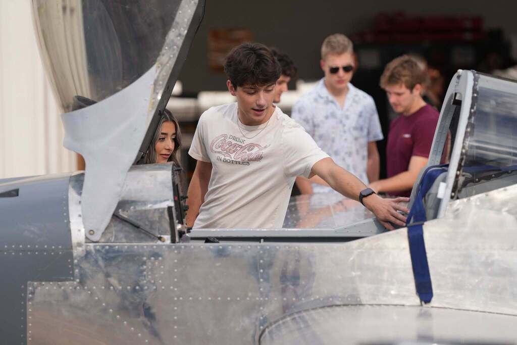 Four individuals are gathered around an airplane, two are inside the cockpit. One man looks out of the cockpit.