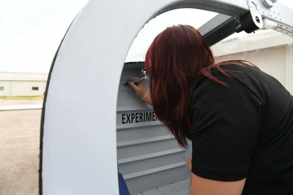 Person in a black shirt with red hair writing on a white and gray mobile unit labeled "EXPERIMENT".